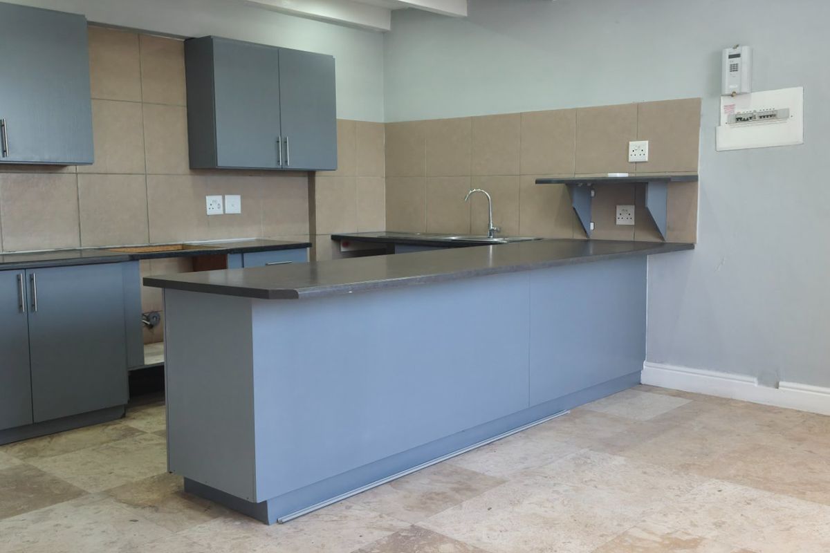 A functional kitchen featuring grey cabinetry, dark countertops, a stainless steel sink, and tiled flooring. The space is currently vacant and ready for customization.