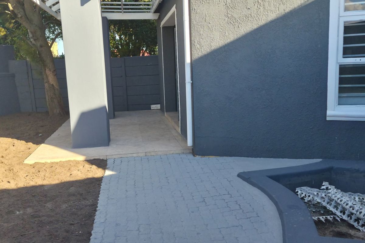 Rear exterior view featuring a tiled patio with a pergola, paved walkway, and boundary wall, showing potential for garden landscaping.