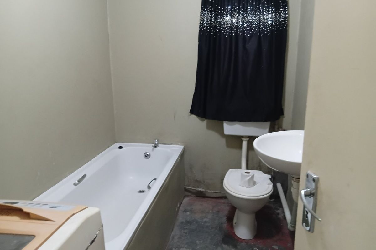 A dated bathroom featuring a standard bathtub, toilet, and pedestal basin, requiring cosmetic updates and floor refinishing to improve its overall condition.