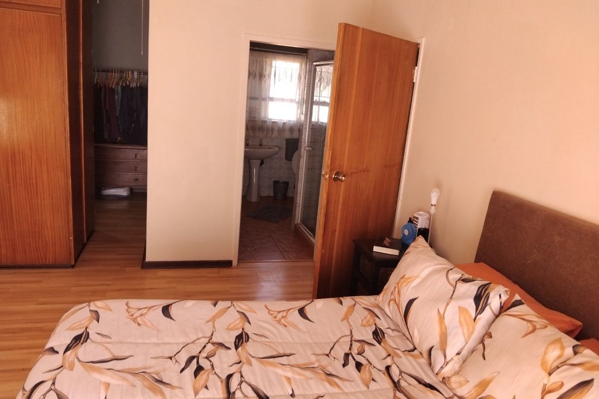 Bedroom featuring laminate flooring and built-in cupboards, with an adjoining en-suite bathroom containing a pedestal basin and shower.