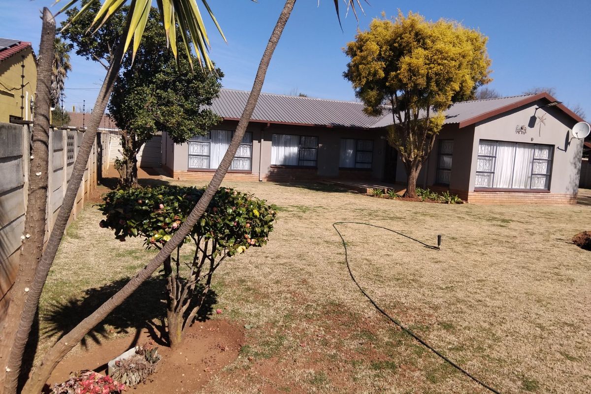 Rear view of the house featuring a spacious lawn, established trees, and a metal roof with aluminium window frames.