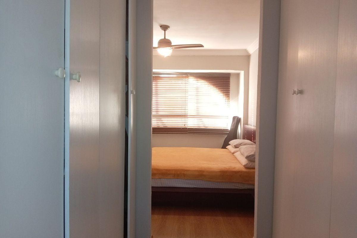 A bedroom viewed from a hallway, featuring built-in cupboards, laminate flooring, and a ceiling fan.