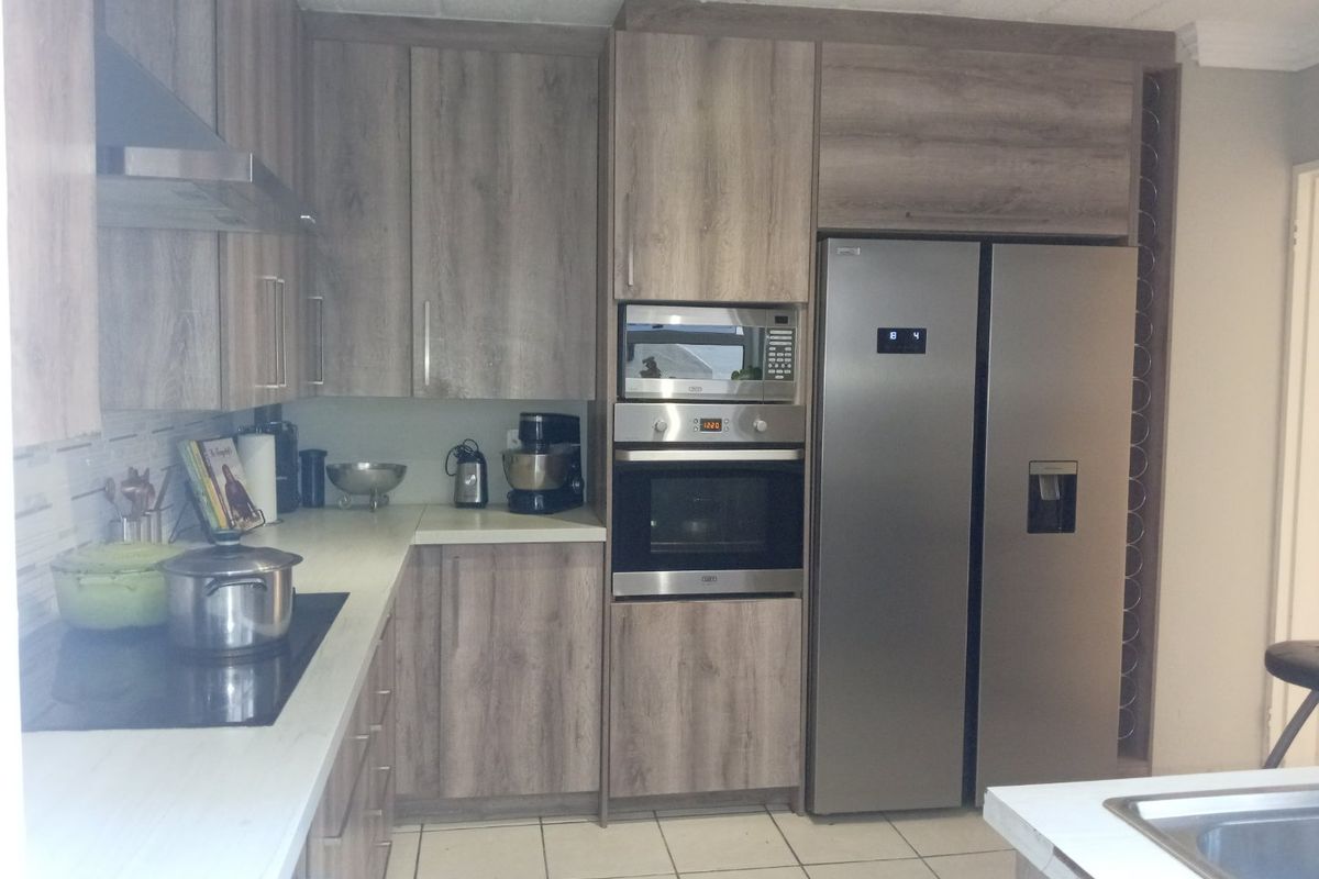 A functional kitchen featuring wood-look cabinetry, integrated stainless steel appliances, electric hob, and tiled flooring.