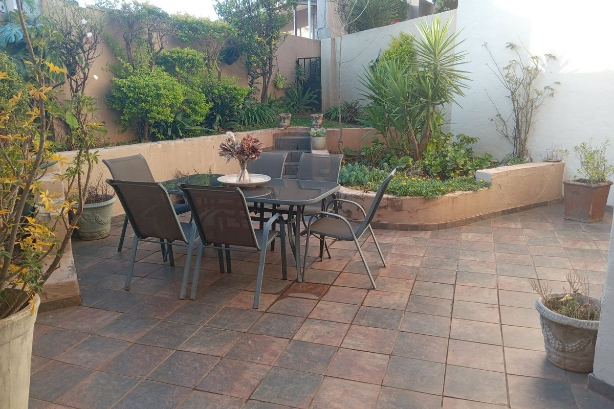 A private rear courtyard featuring a tiled patio area, tiered garden beds with retaining walls, and established landscaping.