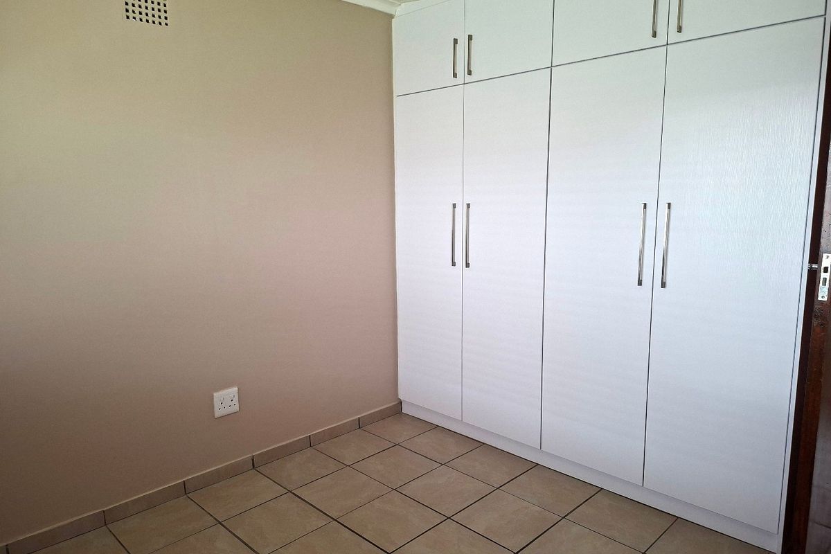 A clean, empty bedroom featuring neutral wall tones, tiled flooring, and ample built-in cupboard storage.