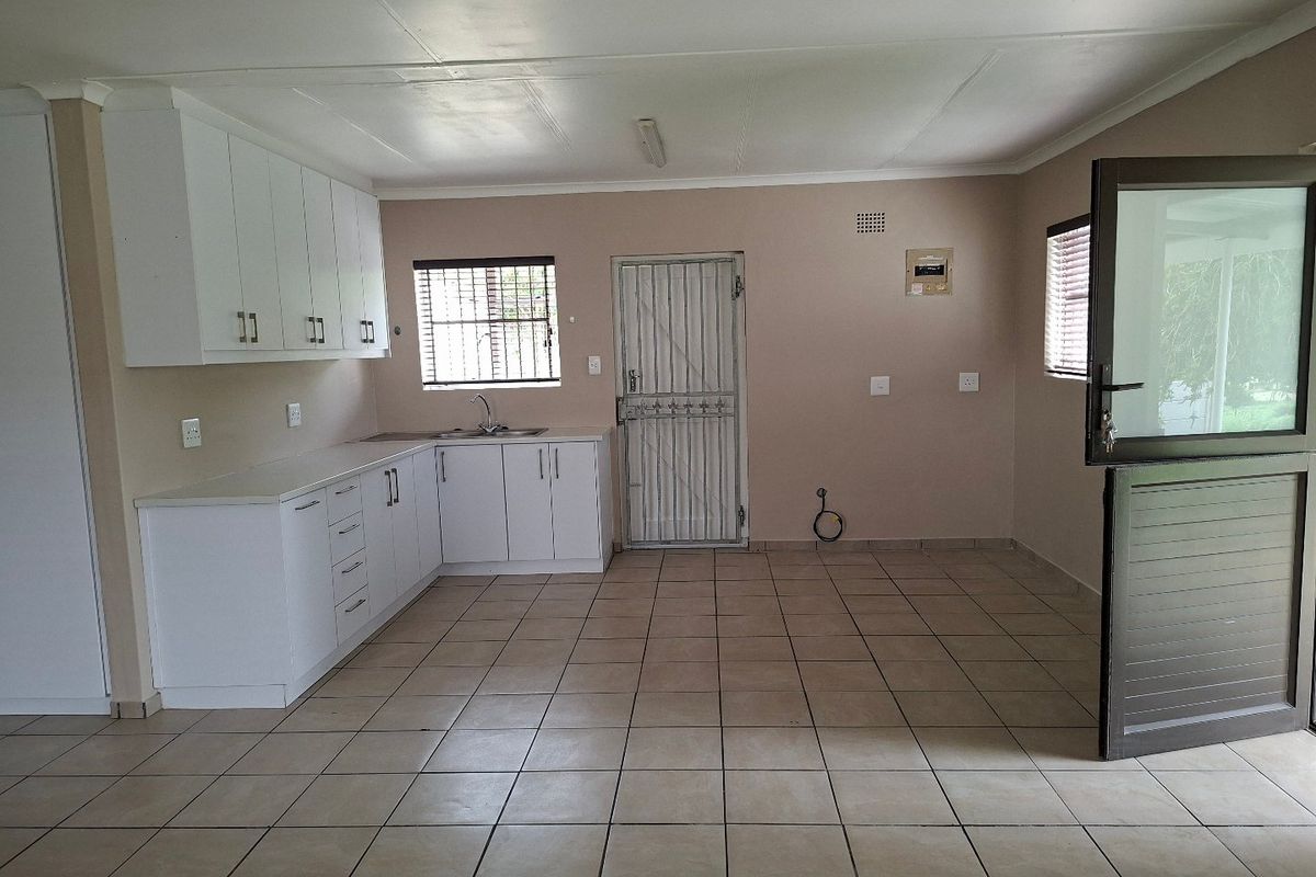 A clean, empty kitchen featuring white cabinetry, tiled flooring, and a secure stable door leading to the exterior.