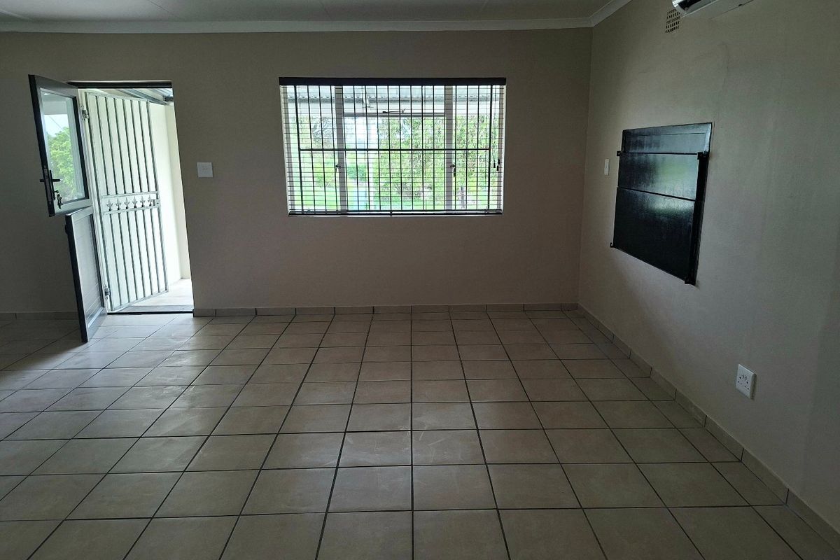 An empty living room featuring tiled flooring, a wall-mounted air conditioning unit, and security bars on the window and door.