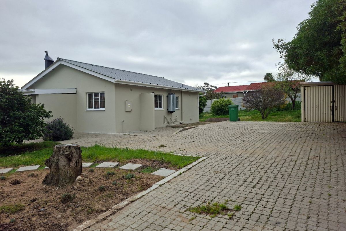 Rear view of the property featuring a paved driveway, metal roofing, external geyser, and a detached corrugated metal storage shed.