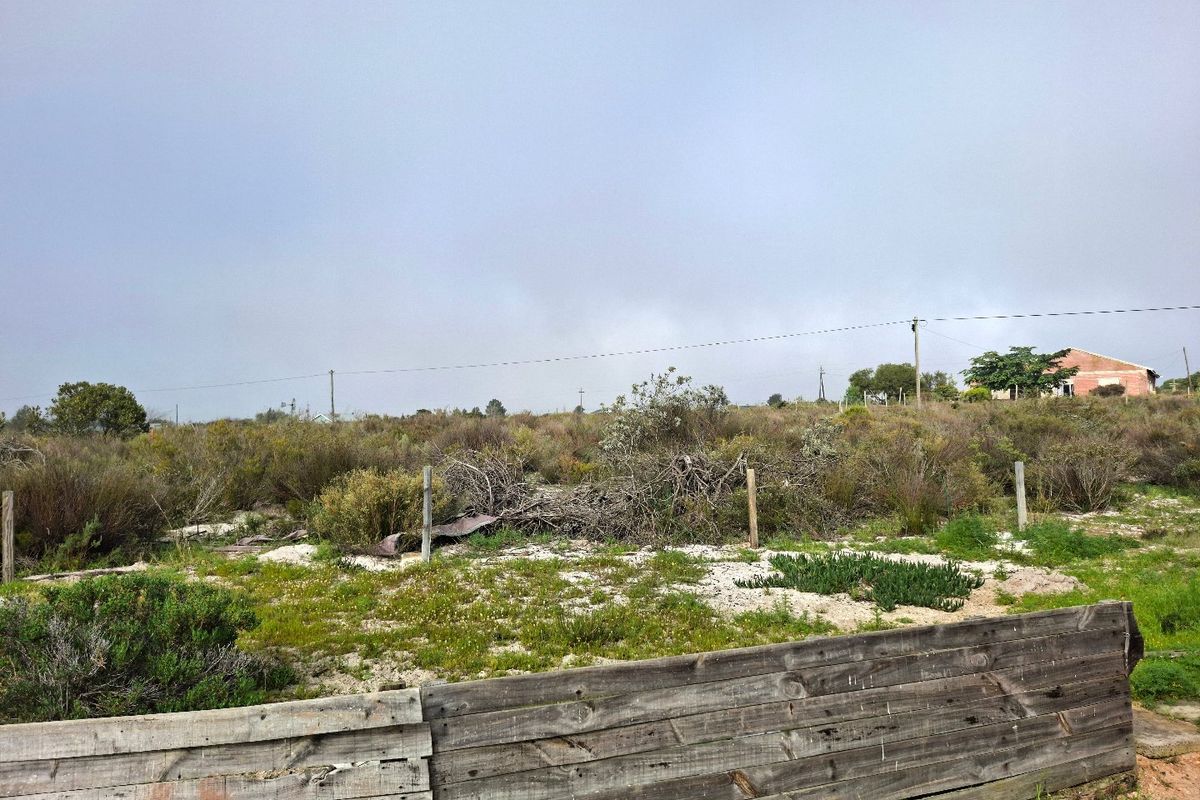 A vacant residential plot featuring natural vegetation, a wooden perimeter fence, and overhead power lines, offering a blank canvas for future development.