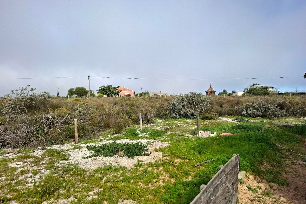 A view of a vacant residential plot featuring natural vegetation, sandy soil, and existing boundary fence posts.