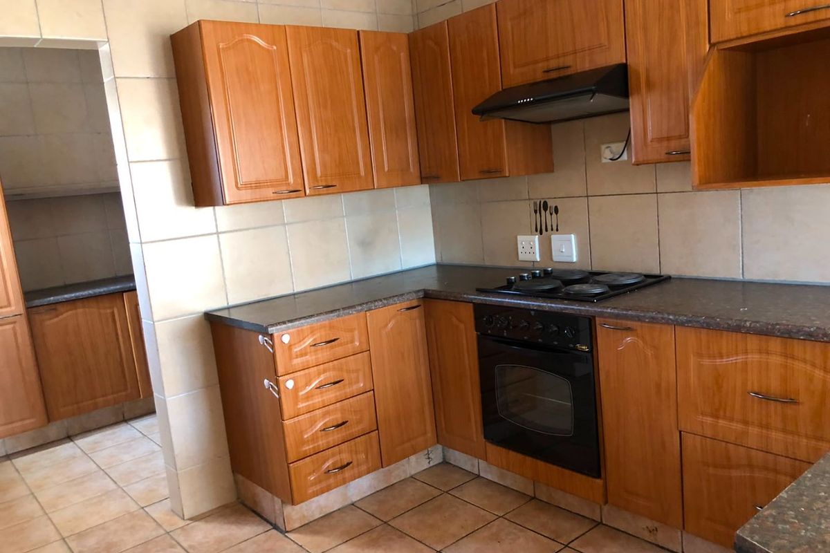 Functional kitchen featuring wood-look cabinetry, built-in oven, electric hob, extractor fan, and tiled splashbacks with an adjacent scullery area.