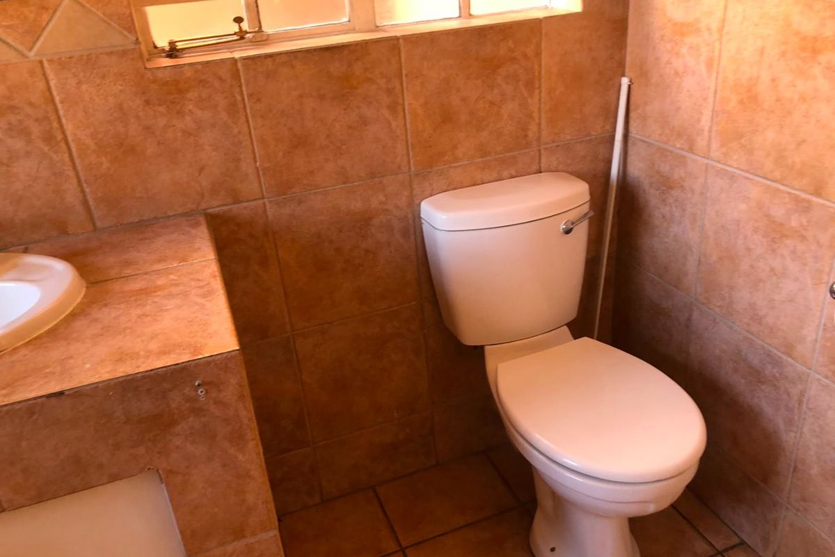 A compact bathroom featuring floor-to-ceiling terracotta-style tiling, a built-in tiled vanity with basin, and a standard toilet.