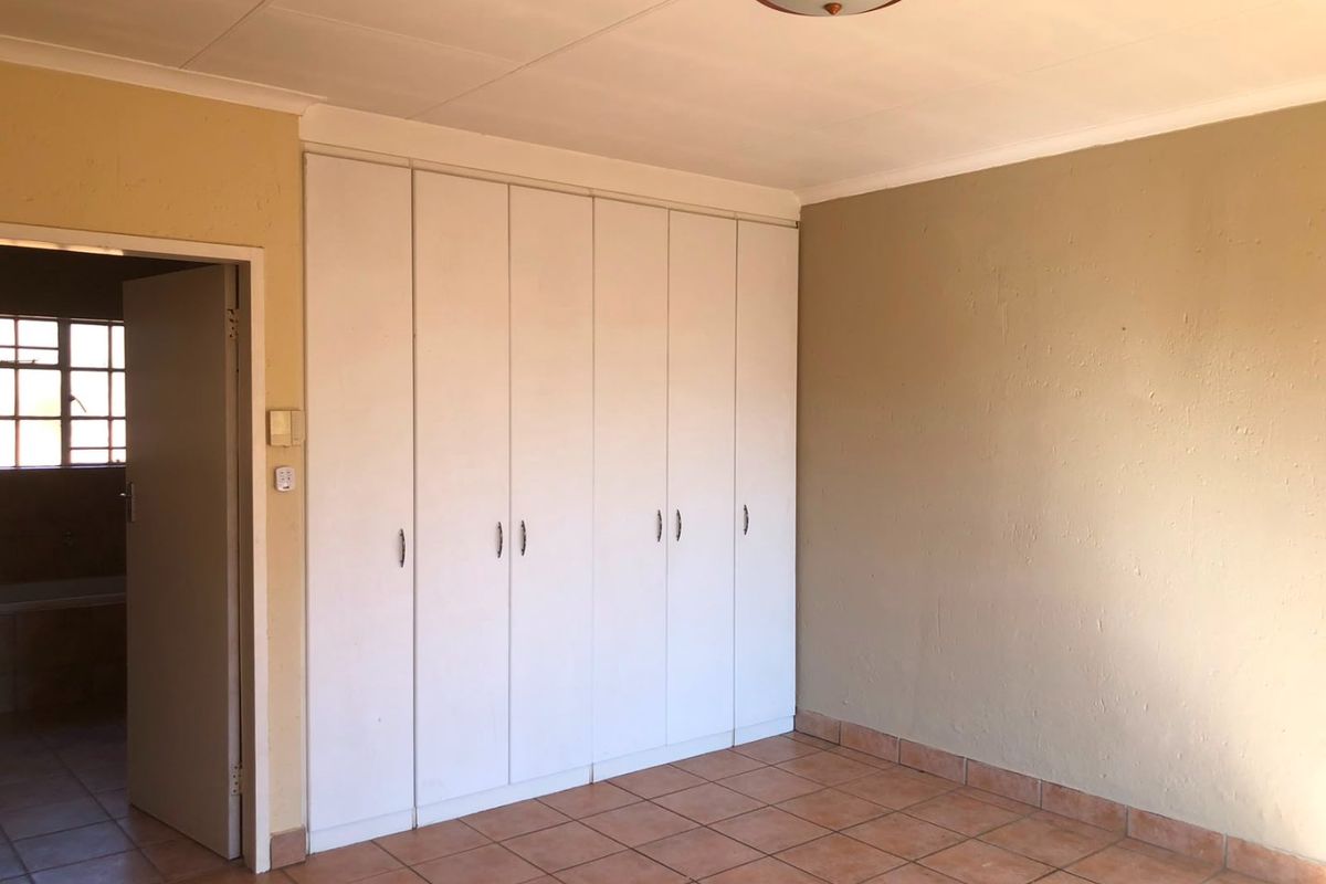 A spacious bedroom featuring built-in cupboards, tiled flooring, and neutral wall tones, offering a blank canvas for personalization.