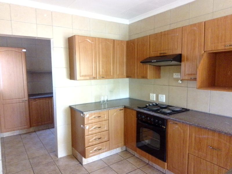 A functional kitchen featuring wood-look cabinetry, built-in oven and hob, tiled splashbacks, and an adjoining scullery area.