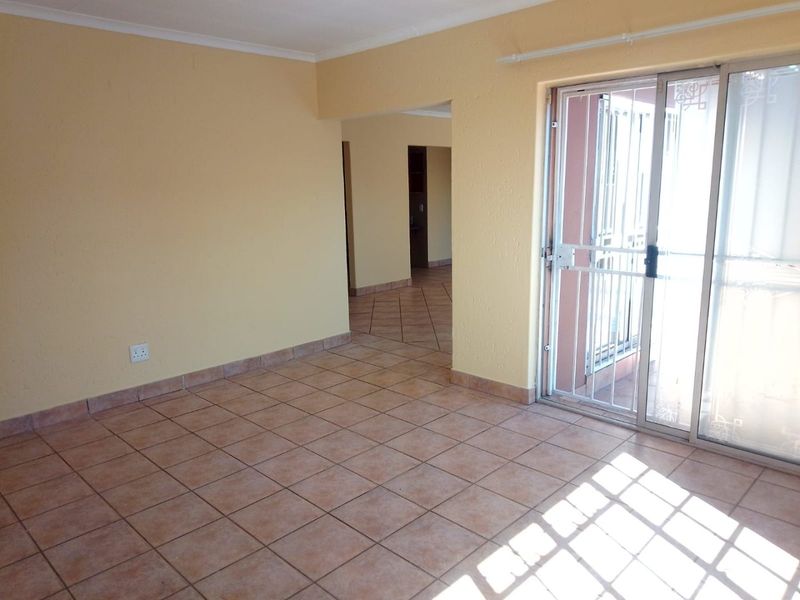 An empty living room featuring ceramic floor tiles, coved ceilings, and a sliding glass door with an integrated security gate leading to the exterior.