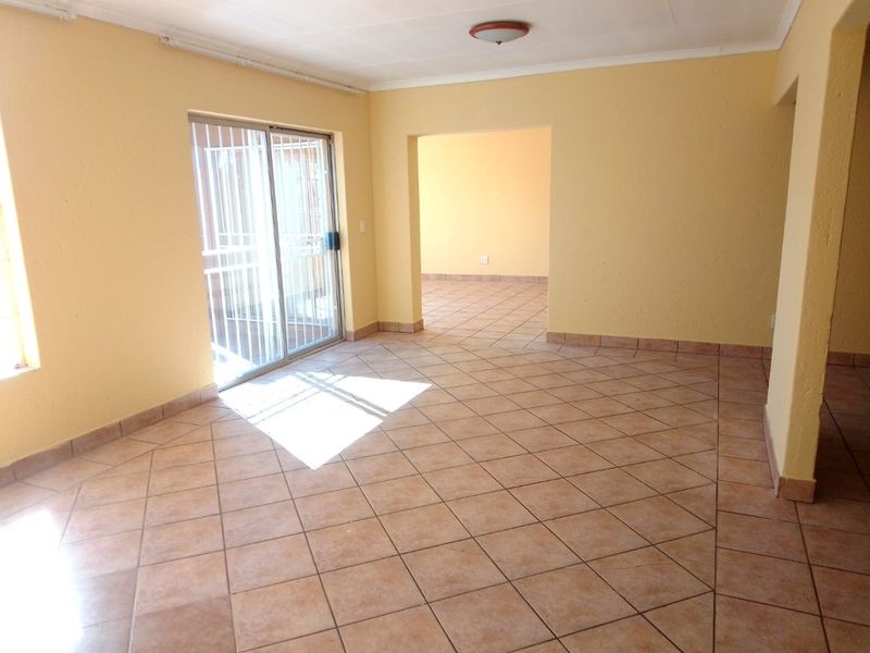An empty, open-plan living area featuring ceramic tile flooring, yellow walls, and a sliding glass door with a security gate leading outside.