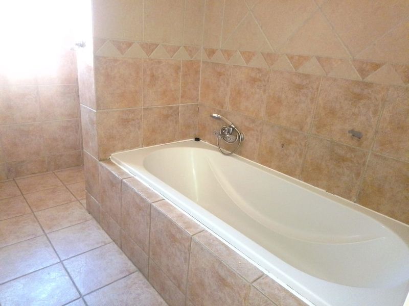 A bathroom featuring a built-in bathtub with a handheld shower mixer, finished with neutral ceramic wall and floor tiles.