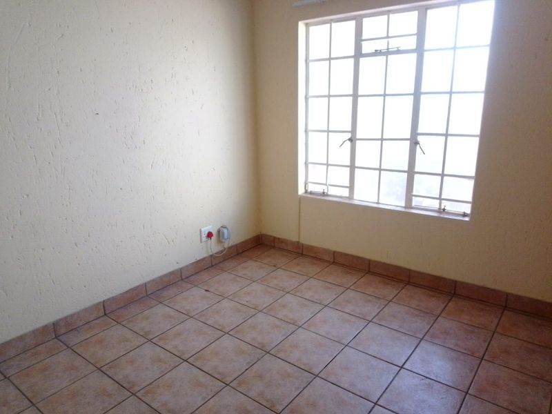 An empty bedroom featuring tiled flooring, textured walls, and a window fitted with security burglar bars.