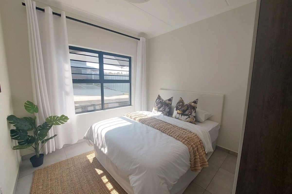 A bright and well-maintained bedroom featuring tiled flooring, neutral walls, and a large aluminium-framed window allowing for natural light.