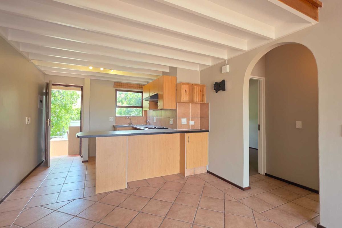 Open plan kitchen and living area featuring tiled floors, exposed beam ceilings, and a breakfast bar, leading to an outdoor balcony.