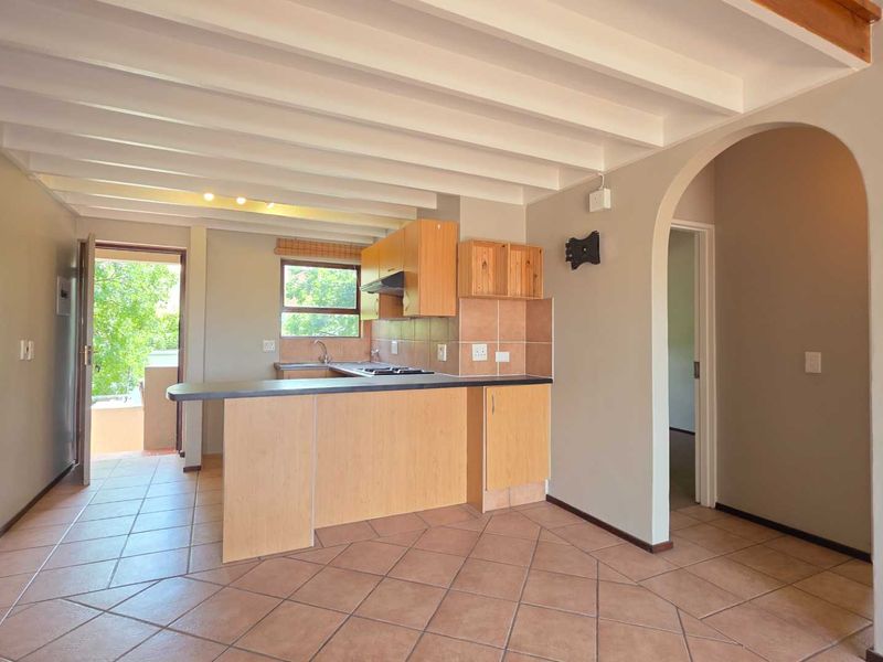 Open plan kitchen and living area featuring tiled floors, exposed beam ceilings, and a breakfast bar, leading to an outdoor balcony.