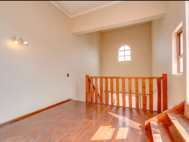An empty landing area featuring wooden flooring, a wooden balustrade, and an arched window, providing a bright and open transition space.