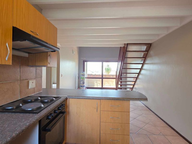 Open plan kitchen and living area featuring wooden cabinetry, tiled floors, exposed beam ceilings, and a staircase leading to an upper level.