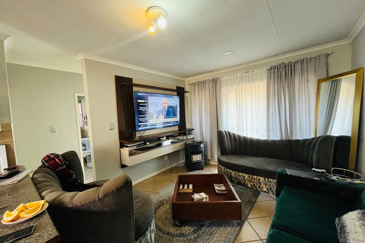 A comfortable living room featuring a built-in media console, tiled flooring, and large windows with curtains, providing a functional and well-lit space.