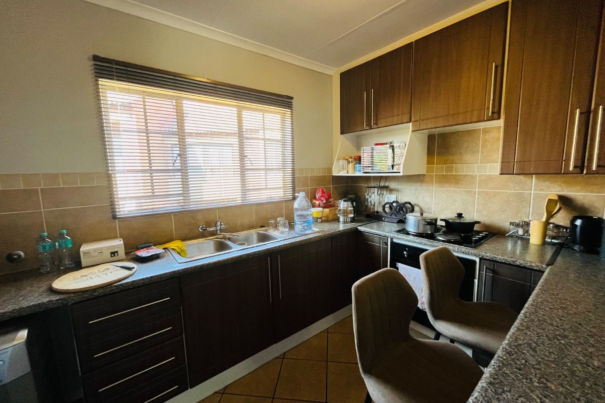 A functional kitchen featuring dark wood cabinetry, granite countertops, a double basin sink, and built-in cooking appliances with a tiled backsplash.