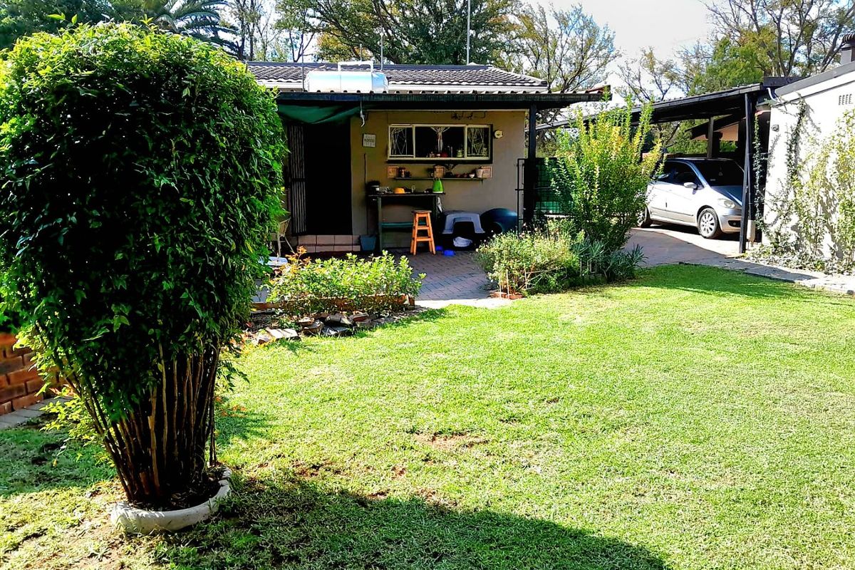 A rear view of the property featuring a well-maintained lawn, a paved patio area, and a covered carport for vehicle storage.