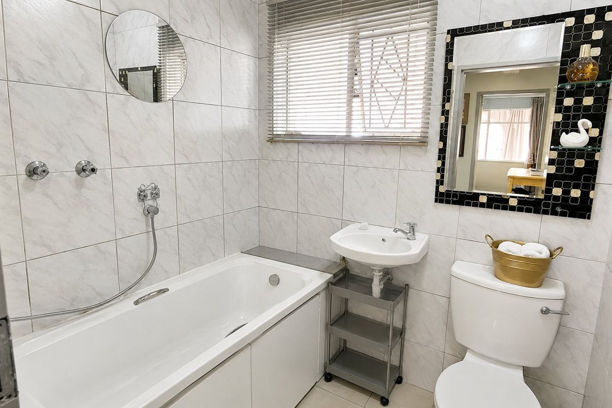 A functional bathroom featuring a built-in bathtub, wall-mounted shower mixer, pedestal washbasin, and toilet with tiled wall finishes.