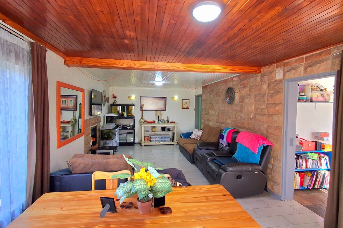 Spacious living area featuring a timber tongue and groove ceiling, stone feature wall, and tiled flooring, offering a rustic and comfortable atmosphere.