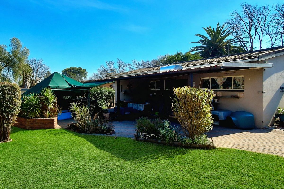 Rear view of the property featuring a paved patio area, established garden with lawn, and a solar water heating system installed on the roof.