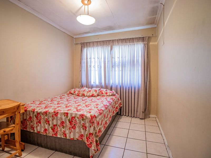 A bedroom featuring tiled flooring and a ceiling light fixture, currently showing signs of wear including ceiling water staining and scuffed wall finishes.