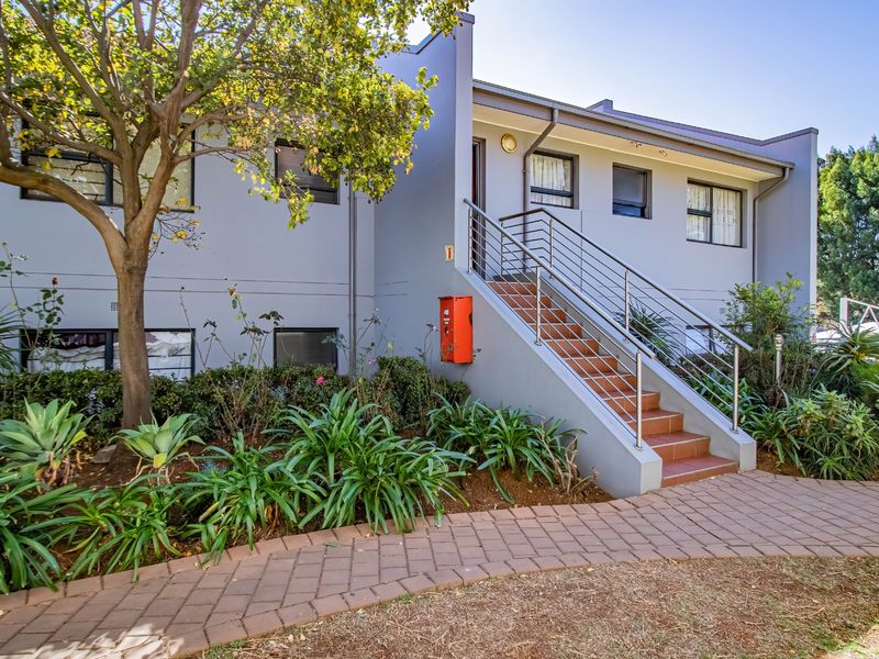 Front exterior view of the apartment building featuring a paved walkway, landscaped garden, and a staircase leading to the entrance.