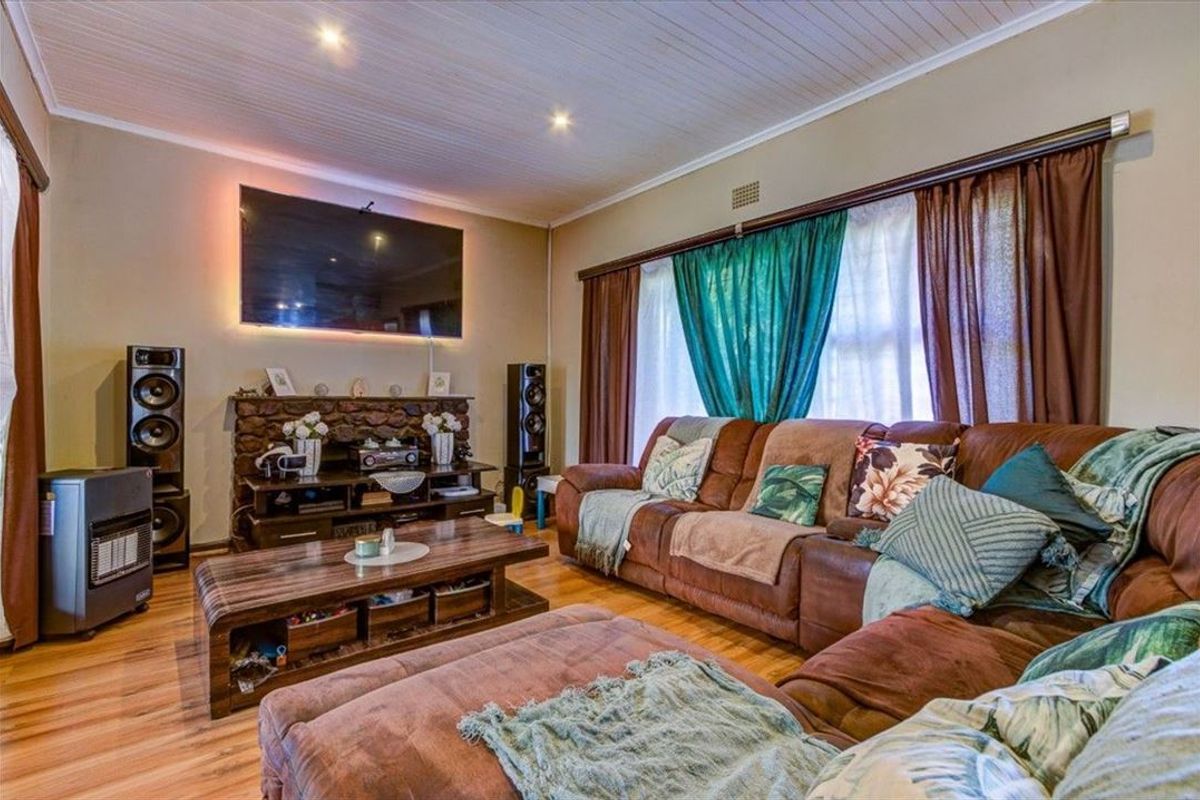 A cozy living room featuring a stone fireplace, laminate flooring, and a tongue and groove ceiling with recessed lighting.