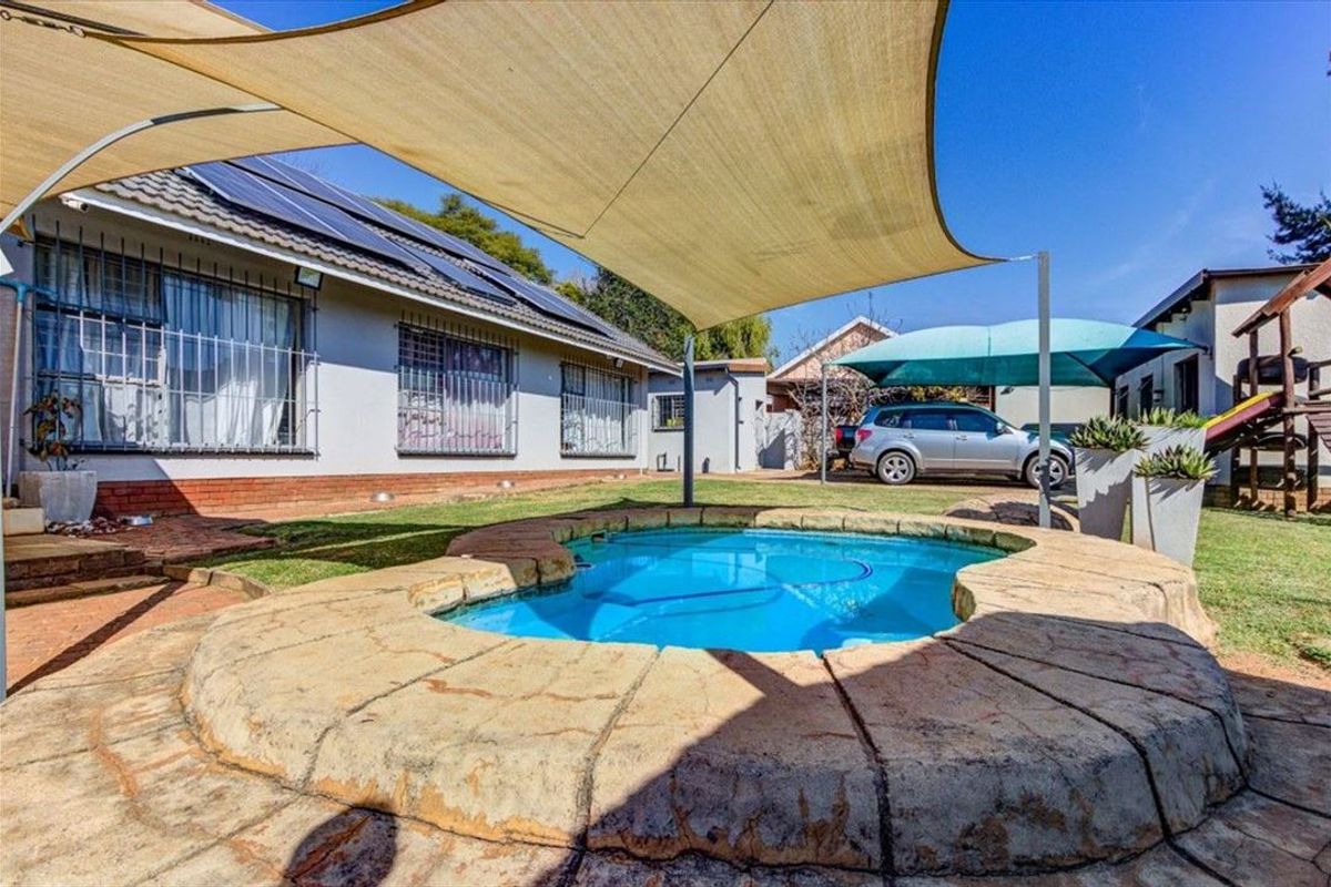 Outdoor pool area featuring a paved surround, shade sail, and views of the rear garden and house exterior with solar panels.