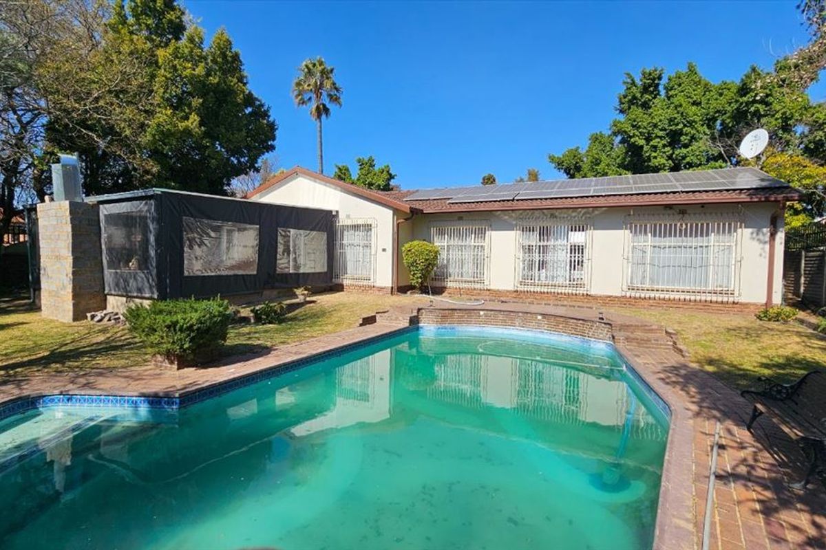 Rear garden featuring a swimming pool, brick paved surround, and a house exterior equipped with roof-mounted solar panels and security bars on windows.