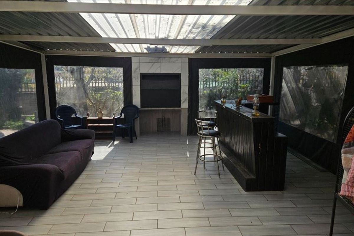 Covered outdoor patio featuring a built-in braai, tiled flooring, and roll-up canvas blinds, creating a versatile entertainment space.