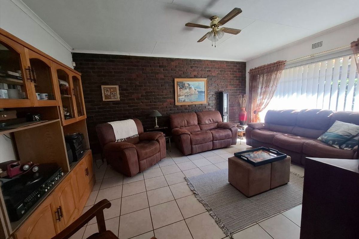 A living room featuring an exposed brick accent wall, tiled flooring, and a ceiling fan, offering a traditional layout with natural light.