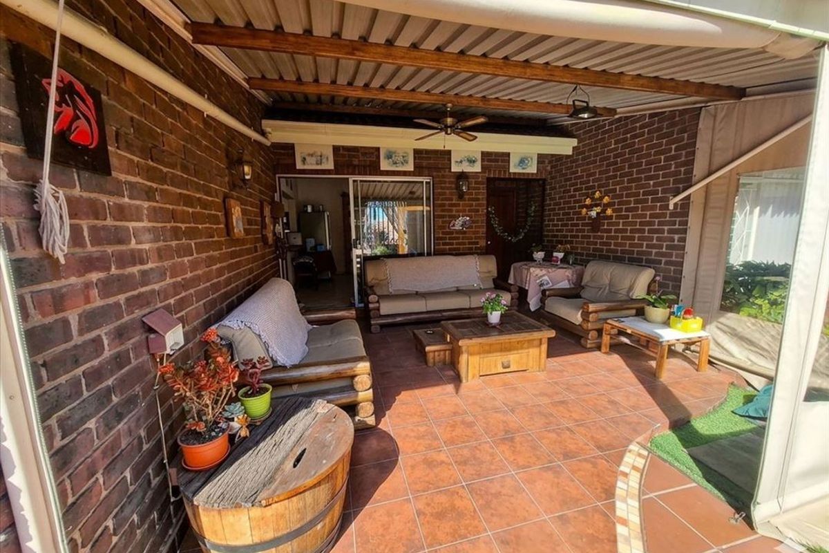 A covered outdoor patio featuring exposed brick walls, tiled flooring, and a ceiling fan, providing a functional space for outdoor relaxation.