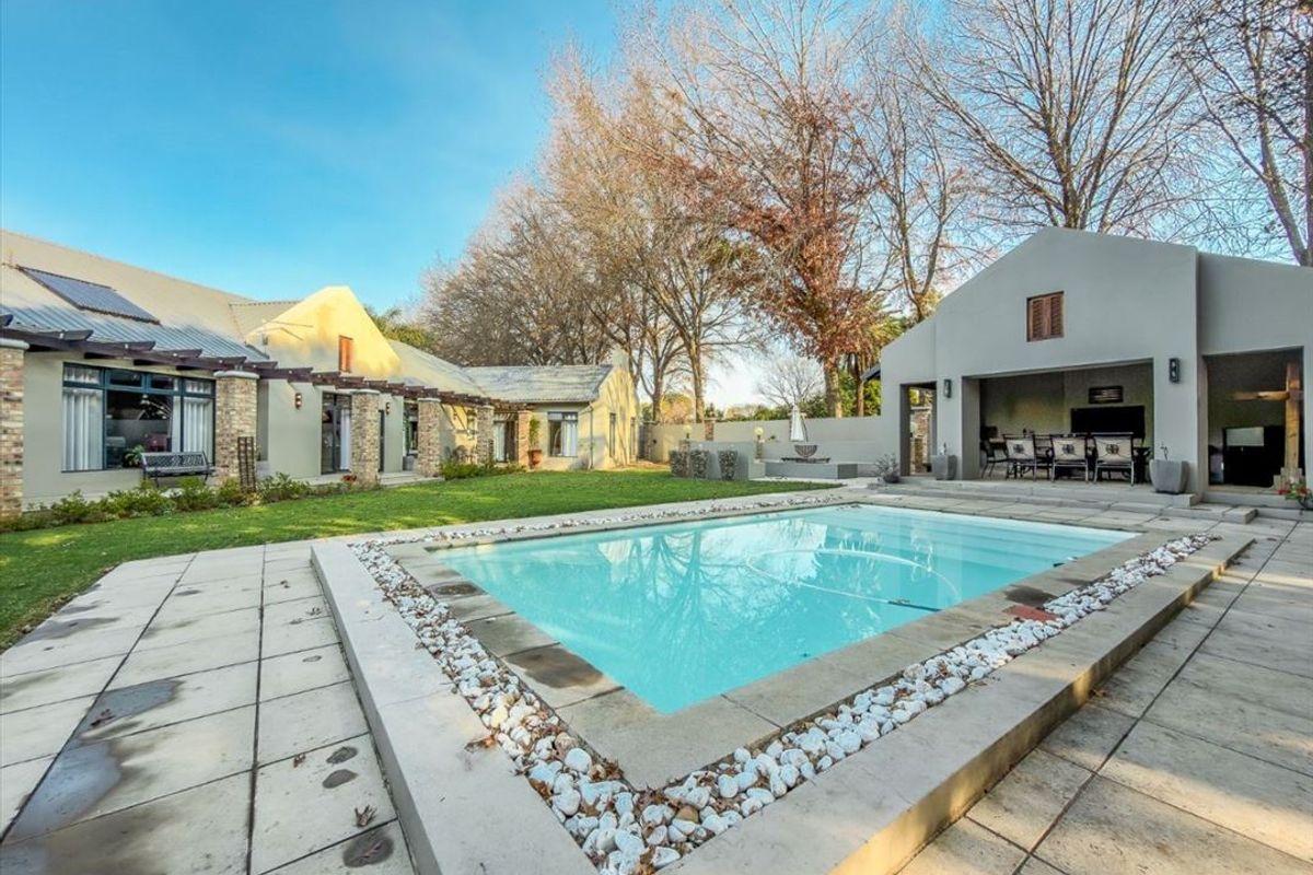 Spacious outdoor entertainment area featuring a swimming pool, stone-paved surround, and a covered patio structure set within a landscaped garden.
