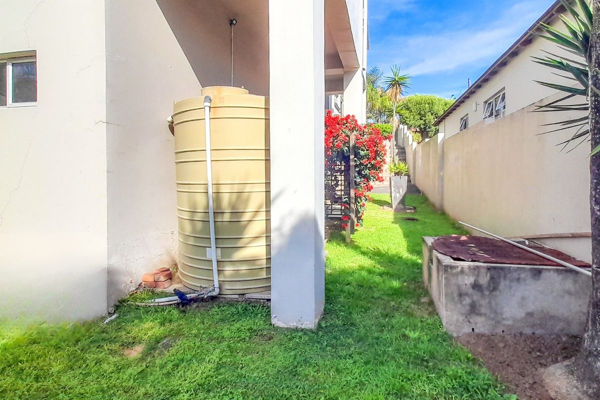 Rear exterior area featuring a water storage tank, concrete utility structure, and boundary wall with lawn space.
