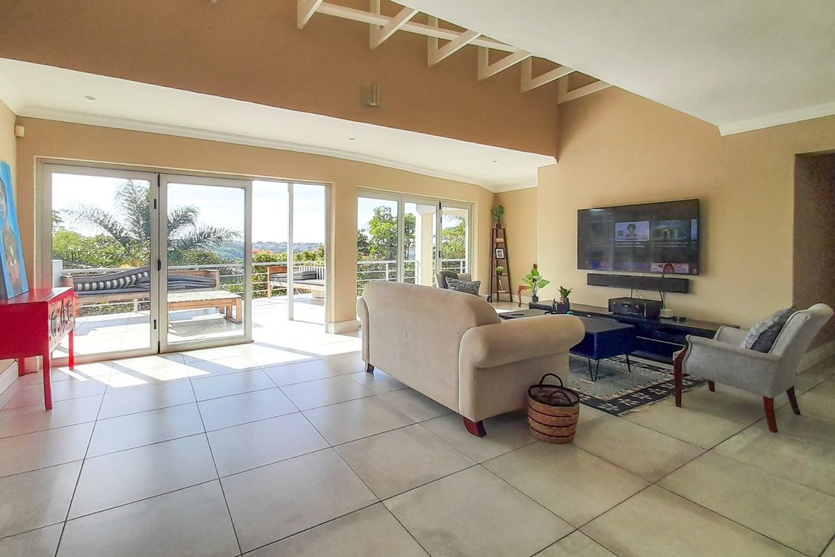 Spacious living room featuring tiled flooring, exposed rafters, and large sliding glass doors that provide seamless access to the outdoor patio area.
