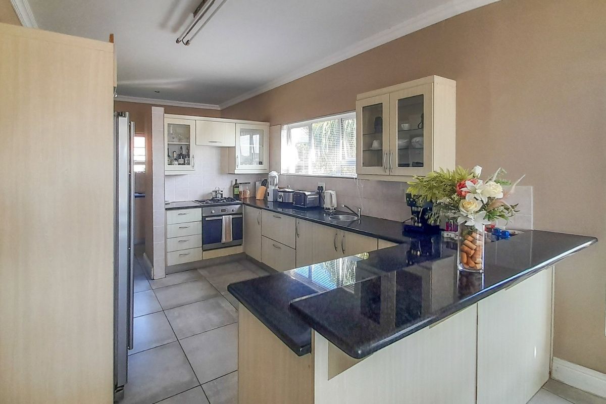 A functional kitchen featuring granite countertops, built-in cabinetry, a gas hob, and an integrated oven, with tiled flooring throughout.