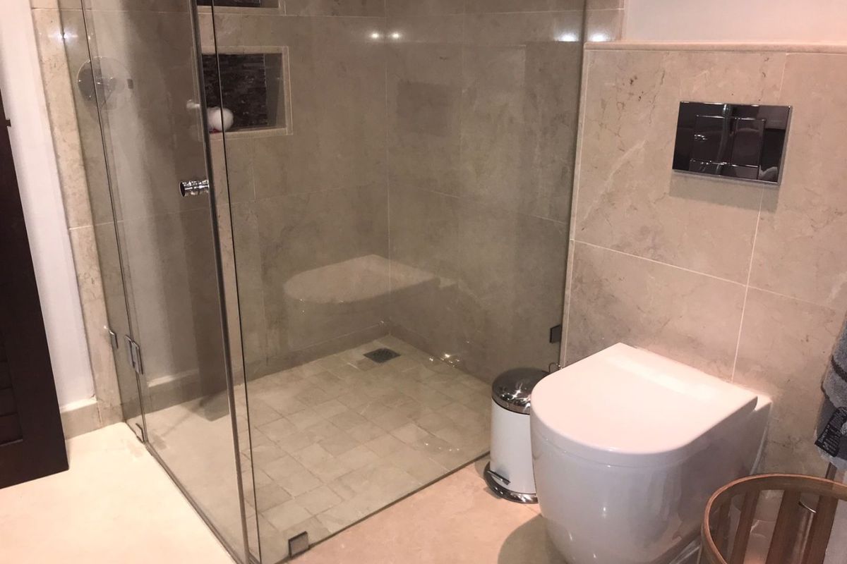 Modern bathroom featuring a glass-enclosed shower with recessed niches and a wall-mounted toilet with stone wall tiling.