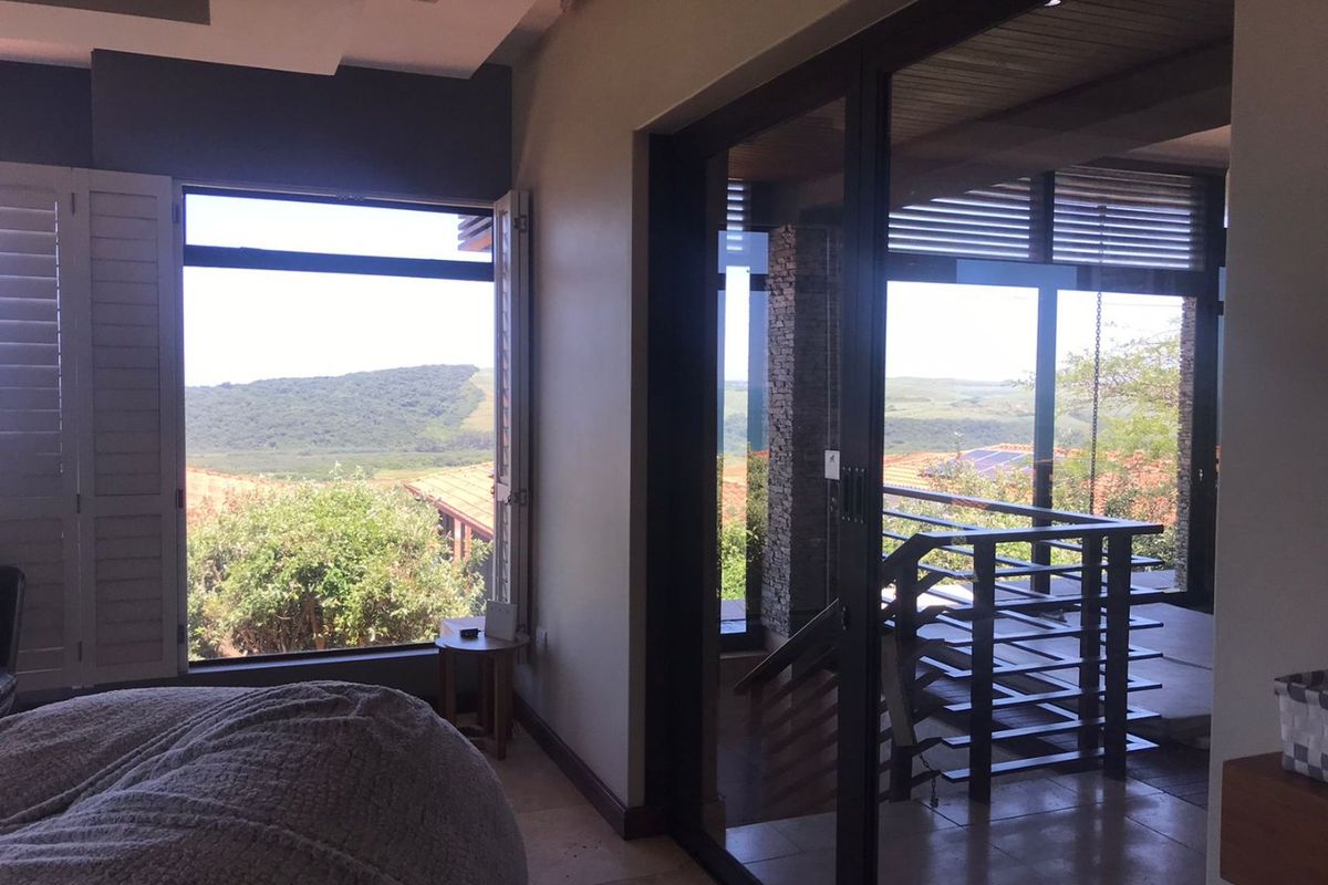 Spacious bedroom featuring large sliding glass doors, plantation shutters, and direct access to a balcony with scenic landscape views.