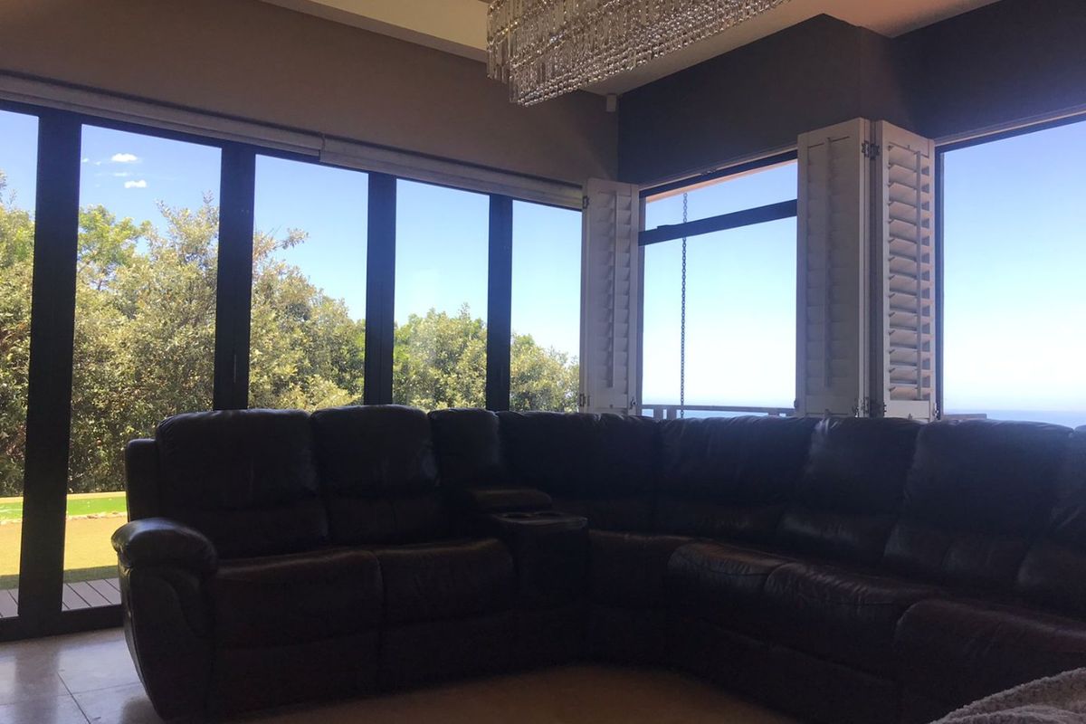 Spacious living area featuring large floor-to-ceiling glass doors, plantation shutters, and a prominent crystal chandelier, offering abundant natural light and garden views.