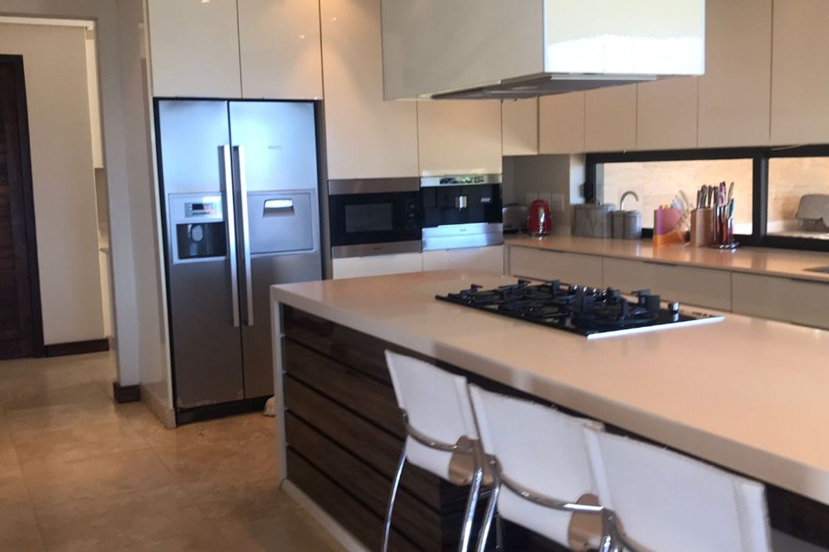 Modern kitchen featuring a large island with gas cooktop, sleek gloss cabinetry, stone countertops, and integrated appliances in a contemporary open-plan layout.