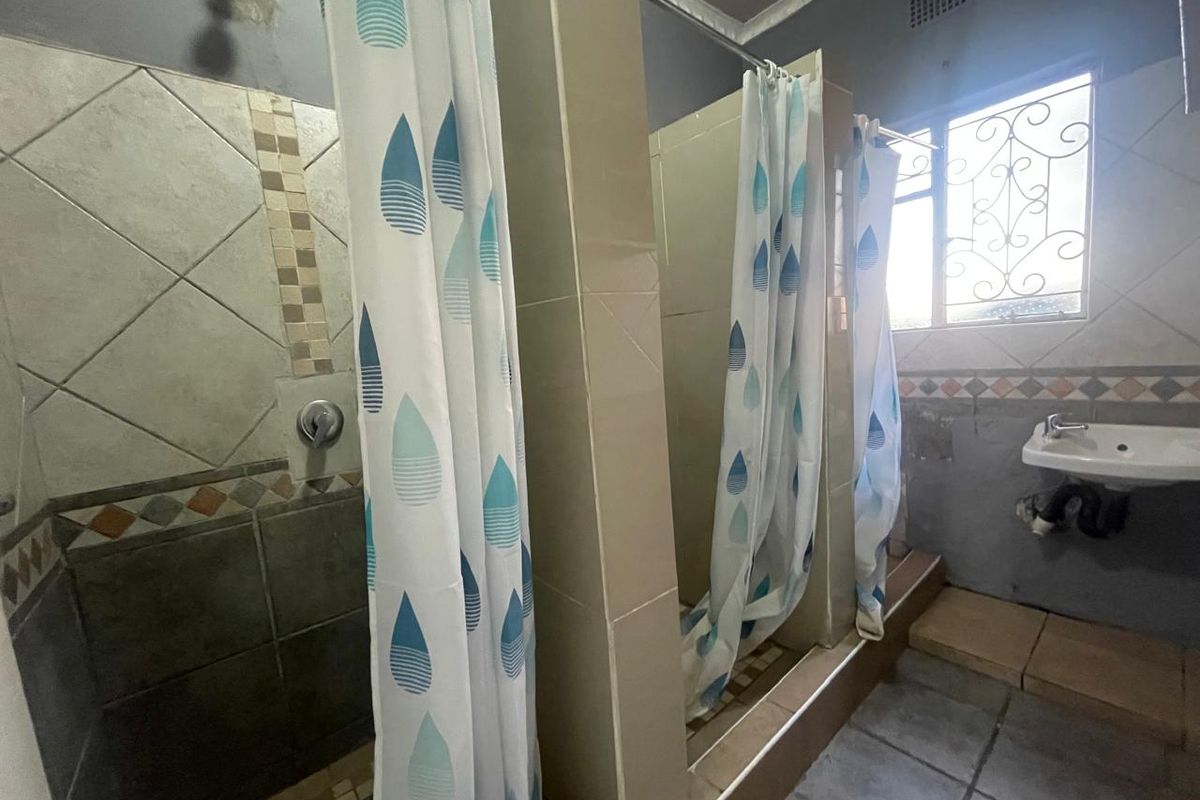 A functional bathroom featuring multiple shower stalls with curtain enclosures and a wall-mounted basin, requiring cosmetic updates to finishes and fixtures.